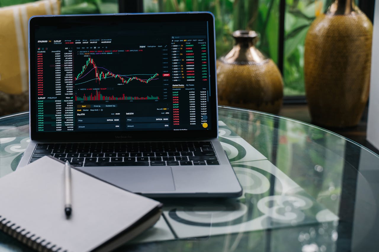 Crafting Captivating Headlines: Your awesome post title goes here Laptop displaying cryptocurrency stocks and graphs on a glass table with a notepad.